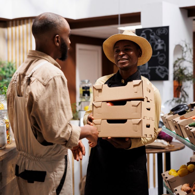 Smiling African American man, the owner of modern supermarket, offers a variety of eco friendly organic products. The shelves are filled with fresh produce, glass jars and reusable packaging options.